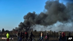 People walk as a cloud of smoke raises after an explosion near the airport, in Lviv, western Ukraine, March 18, 2022.