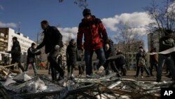 La gente limpia los escombros fuera de un centro médico dañado después de que partes de un misil ruso, derribado por la defensa aérea ucraniana, aterrizaran en un bloque de apartamentos cercano, según las autoridades, en Kiev, Ucrania, el 17 de marzo de 2022.