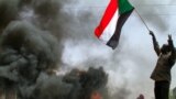 FILE: A man waves a national flag near burning tiresd as Sudanese demonstrators in the capital, Khartoum, to protest last year's military coup by General Abdel Fattah al-Burhan and the emergency order he imposed to try to control protests and dissent. Taken March 24, 2022. 