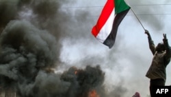 FILE: A man waves a national flag near burning tiresd as Sudanese demonstrators in the capital, Khartoum, to protest last year's military coup by General Abdel Fattah al-Burhan and the emergency order he imposed to try to control protests and dissent. Taken March 24, 2022. 