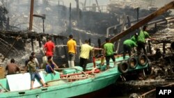 Para pekerja dan petugas pemadam kebakaran mencoba memadamkan api yang melahap kapal-kapal nelayan di Pelabuhan Benoa, Bali, 9 Juli 2018.