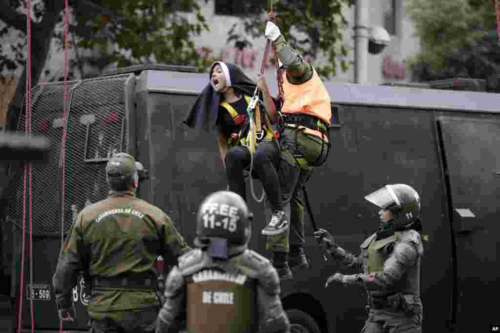 An activist dressed as a nun is lowered by a police officer, and detained, after she and other protesters placed a pro-abortion banner above a road near Pope Francis' expected route, before the pontiff's arrival in Santiago, Chile, Jan. 15, 2018.
