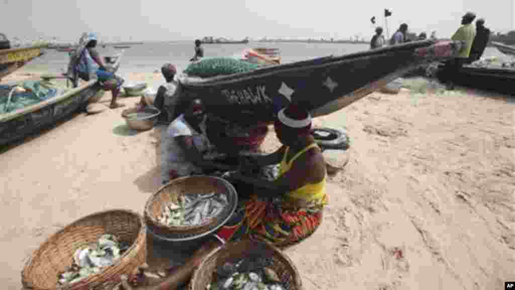 Women sit in the shade of a fishing boat as they prepare fish for sale, at Takwabay beach, Nigeria.