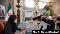 Une mère vote lors de la présidentielle iranienne dans un bureau de vote du consulat iranien, à Najaf, en Irak, le 18 juin 2021.