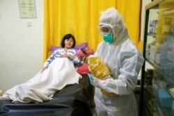 Seorang perawat dengan mengenakan alat pelindung diri untuk mencegah penularan virus corona sedang menggendong bayi yang baru lahir di kamar bersalin di Depok, 13 April 2020. (Foto: Reuters)