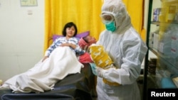 Seorang perawat dengan mengenakan alat pelindung diri untuk mencegah penularan virus corona sedang menggendong bayi yang baru lahir di kamar bersalin di Depok, 13 April 2020. (Foto: Reuters)