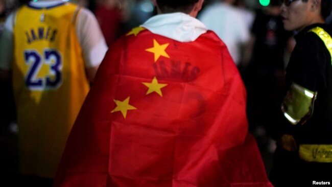 中国上海,在NBA布鲁克林篮网队和洛杉矶湖人队的表演赛之前,一名身穿勒布朗·詹姆斯球衣的男子在梅赛德斯-奔驰球场外用中国国旗包裹自己。(2019年10月10日)。