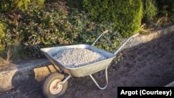Single wheel garden wheelbarrow loaded with crushed stone prepared for garden path reconstruction in the autumn garden