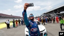 El conductor Bubba Wallace se se hace un autorretrato con su teléfono junto a sus compañeros, quienes empujaron su auto al frente de la Pista Talladega antes del inicio de la carrera de autos de la Copa NASCAR el 22 de junio de 2020.