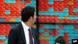 FILE - People walk past an electronic stock board showing Japan's Nikkei 225 index at a securities firm in Tokyo, Nov. 7, 2018. 