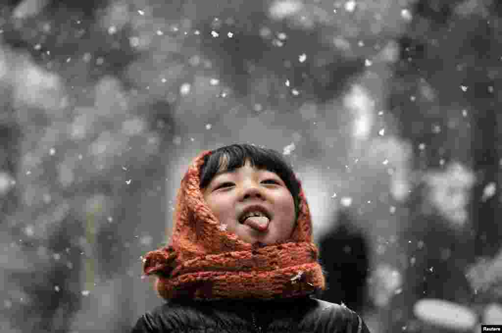 A girl sticks out her tongue during a snowfall on a street in Hefei, Anhui province, China.