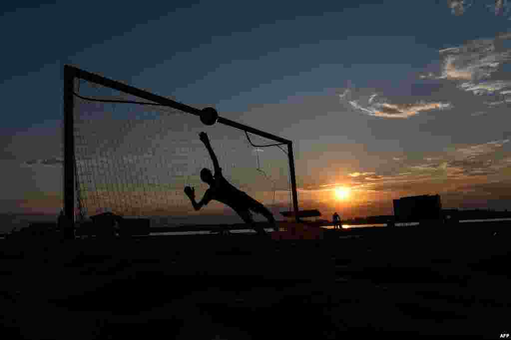 A young Russian boy plays football on the banks of the Volga river as the sun sets in Samara.