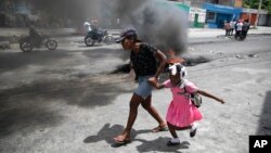 FILE - A woman guides a child past a demonstration against increasing violence in Port-au-Prince, Haiti, March 29, 2022.