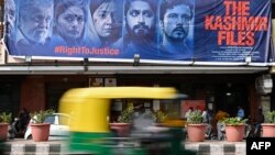 An auto rickshaw moves past a banner of Bollywood movie "The Kashmir Files" installed outside a cinema hall in the old quarters of Delhi, March 21, 2022.
