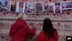 FILE: Family members write a message to two sisters who died of COVID on the National Covid Memorial wall in London, March 29, 2022.