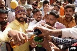 Para pengunjung saling berbagi minuman keras setelah prasad (sesajen miras) tersebut merka bawa ke kuil Baba Rode Shah di desa Bhoma, sekitar 35 kilometer dari Amritsar, 24 Maret 2022. (Narinder NANU / AFP)