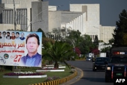 Motorists ride past a banner featuring an image of Pakistan's Prime Minister Imran Khan beside the Parliament building in Islamabad, March 31, 2022.