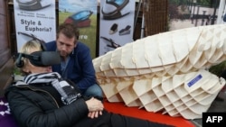  FILE - Dutch designer Alexander Bannink explains how the ‘Sarco’ euthanasia pod works as a woman experiences sitting in the device by wearing virtual reality glasses, on April 14, 2018 at the Amsterdam Funeral Expo. 