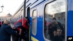 2022年3月23日，在乌克兰南部的奥德萨火车站，一名男子帮助一名残疾的乌克兰老人上火车，车内一个小孩向外挥手。（美联社）