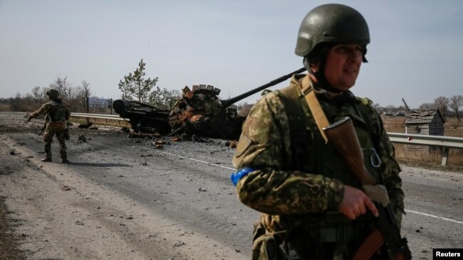 A Ukrainian serviceman stands near the wreck of a Russian tank on the front line in the Kyiv region, Ukraine March 28, 2022. (REUTERS/Gleb Garanich)