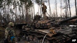 ယူကရိန်းစစ်သည်များ Ukrainian soldiers stands one top of a destroyed Russian tank on the outskirts of Kyiv, Ukraine, March 31, 2022. 