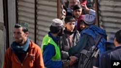 A Taliban fighter controls the entrance of people seeking food supplies during a distribution of humanitarian aid for families in need, in Kabul, Feb. 16, 2022.