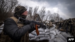 A Ukrainian serviceman holding an assault rifle looks at a Russian drone in a trench at the front line east of Kharkiv on March 31, 2022.