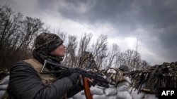 Un militaire ukrainien tenant un fusil d'assaut regarde un drone russe dans une tranchée sur la ligne de front à l'est de Kharkiv le 31 mars 2022.