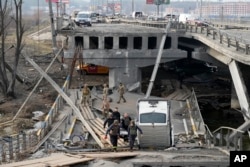Ukrainian soldiers carry a body of a civilian killed by the Russian forces over the destroyed bridge in Irpin close to Kyiv, Ukraine, March 31, 2022.