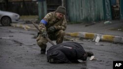 A Ukrainian serviceman checks the dead body of a civilian for booby traps in the formerly Russian-occupied Kyiv suburb of Bucha, Ukraine, April 2, 2022.
