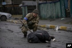 Một quân nhân Ukrainian kiểm tra thi thể một thường dân Ukraine xem có bị gài chất nổ hay không trong khu Bucha ngoại ô Kyiv từng bị Nga chiếm đóng, ở Ukraine, ngày 2 tháng 4, 2022.