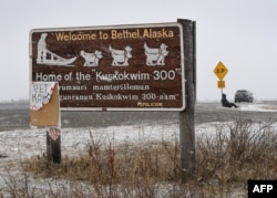 Seorang pria duduk di dekat tanda selamat datang di kota Bethel di Delta Yukon di Alaska pada 16 April 2019. Menurut para ilmuwan, suhu udara di Alaska telah memanas dua kali lebih cepat dari rata-rata global, dengan suhu pada Februari dan Maret memecahkan rekor. (Mark RALSTON/AFP)