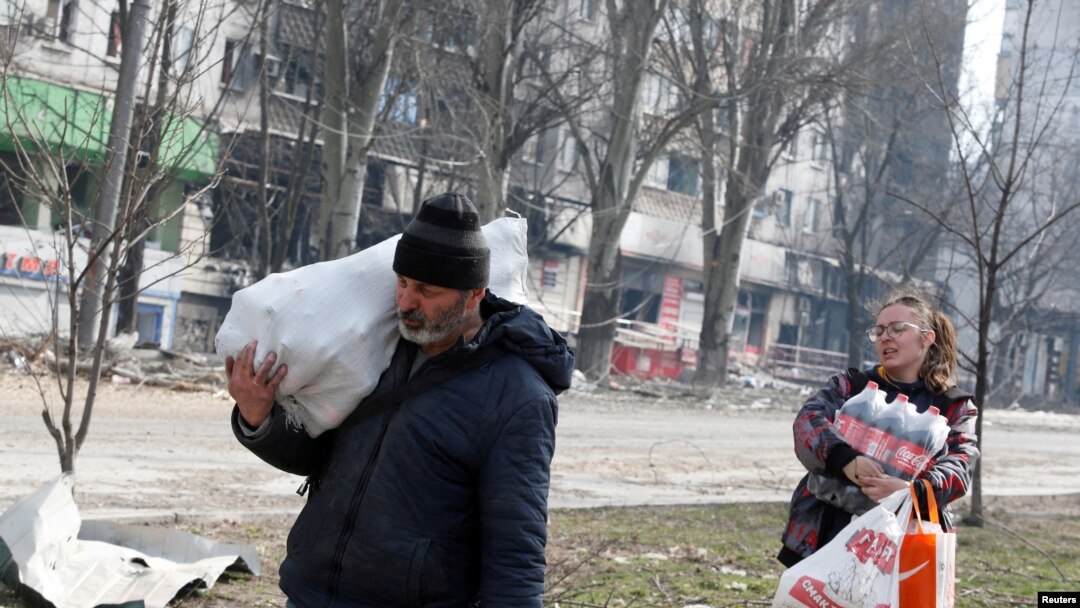 Residentes locales que llevan alimentos pasan frente un edificio de apartamentos dañado por bombardeos rusos en la sitiada ciudad portuaria de Mariupol, en el sur de Ucrania, el 31 de marzo de 2022. REUTERS/Alexander Ermochenko