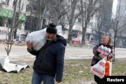 Local residents carry foodstuff while walking past an apartment building damaged during the Russia-Ukraine conflict in the besieged southern port city of Mariupol, Ukraine, March 31, 2022.
