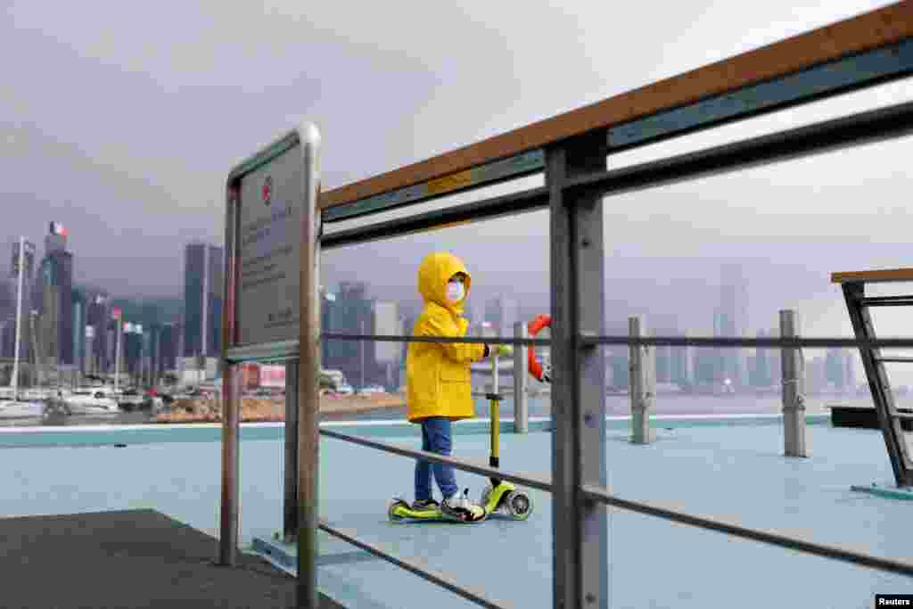 A child wearing a face mask and a raincoat rides a scooter next to Victoria Harbor, amid the COVID-19 pandemic, in Hong Kong, China.