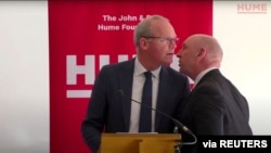 Seorang petugas (kanan) memberi tahu Menlu Irlandia Simon Coveney soal peringatan keamananan saat ia berpidato di Belfast, Irlandia Utara hari Jumat (25/3). 