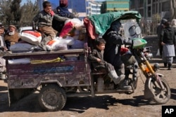 FILE - An Afghan man with his children ride in a three-wheeled vehicle after they received food supplies, during a distribution of humanitarian aid for families in need, in Kabul, Feb. 16, 2022.