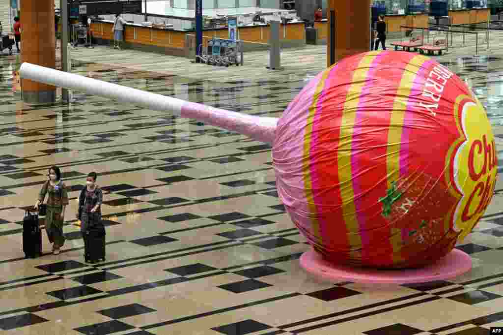 Singapore Airlines stewardesses walk past a giant lollipop candy display at Changi International Airport in Singapore as Singapore reopened its land and air borders to travelers fully vaccinated against COVID-19.