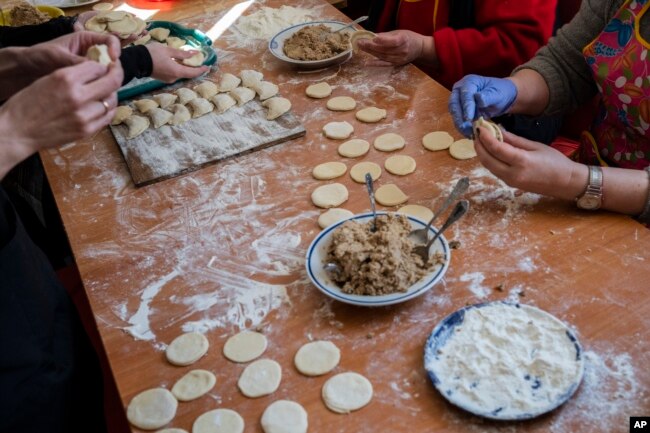 Para sukarelawan menyiapkan varenyky, pangsit isi, di dalam teater di kota Drohobych, Ukraina barat, yang berubah menjadi dapur umum di tengah invasi Rusia ke negara itu, Senin, 21 Maret 2022. (AP / Bernat Armangue)