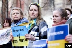 Para pengunjuk rasa memegang gambar kehancuran di Ukraina dalamaksi protes di dekat Perwakilan Tetap Jerman untuk Uni Eropa di Brussels, 11 Maret 2022, meminta Jerman untuk memberikan dukungan segera bagi Ukraina dalam perang melawan Rusia. (Kenzo TRIBOUILLARD / AFP)