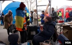 Refugiados ya aturdidos aparecen entre tiendas de campaña y pequeñas carpas y se enfrentan a un desafío de caridad y hospitalidad, lo que al principio se suma a su desorientación, pero cuando se relajan provoca sonrisas. [Jamie Dettmer/VOA]