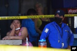 An informal food vendor, left, waits at her stall next to a Municipal Police officer at a crime scene in San Salvador, El Salvador, March 27, 2022.