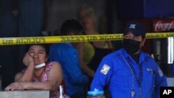 An informal food vendor, left, waits at her stall next to a Municipal Police officer at a crime scene in San Salvador, El Salvador, March 27, 2022.