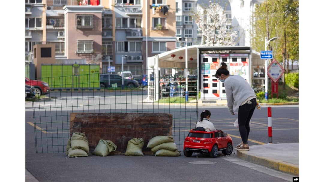 A mother watches as her daughter plays in a toy car next to a barrier set up at the gate of a residential community under lockdown in Shanghai, China, March 29, 2022.