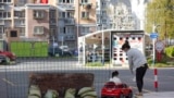 A mother watches as her daughter plays in a toy car next to a barrier set up at the gate of a residential community under lockdown in Shanghai, China, March 29, 2022.