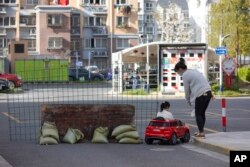 A mother watches as her daughter plays in a toy car next to a barrier set up at the gate of a residential community under lockdown in Shanghai, China, March 29, 2022.
