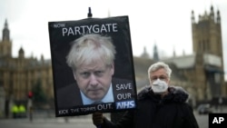 FILE - An anti-Conservative Party protester holds a placard featuring an image of British Prime Minister Boris Johnson with the words "Now Partygate" backdropped by the Houses of Parliament, in London, Britain, Dec. 8, 2021.