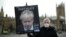 FILE - An anti-Conservative Party protester holds a placard featuring an image of British Prime Minister Boris Johnson with the words "Now Partygate" backdropped by the Houses of Parliament, in London, Britain, Dec. 8, 2021.