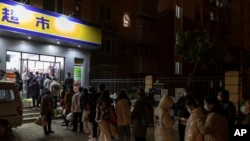 Residents wearing face masks to help protect from the coronavirus line up outside a supermarket at night to buy groceries, March 27, 2022, in Shanghai, China. 