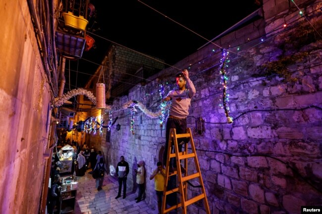 Seorang pria menggantung dekorasi jelang bulan suci Ramadhan di Kota Tua Yerusalem, 29 Maret 2022. (REUTERS/Ammar Awad)